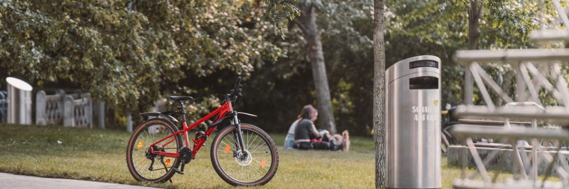 A red bicycle parked in a lush, sunny park with people relaxing nearby in Graz, Austria.